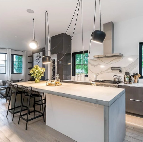 luxury-open-concept-kitchen-remodel-large-waterfall-island Luxury open-concept kitchen remodel with oversized waterfall island, modern pendant lighting, custom cabinetry, and marble backsplash.