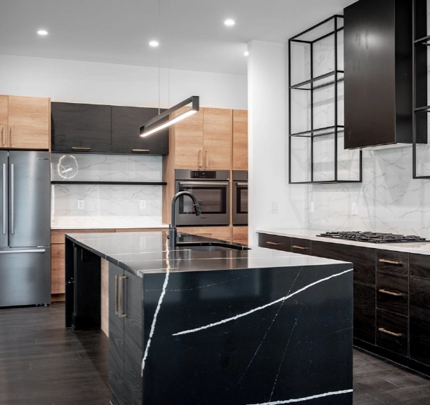 modern-black-marble-kitchen-island-open-concept-design Modern open-concept kitchen featuring dramatic black marble island, mixed wood cabinetry, and contemporary pendant lighting.