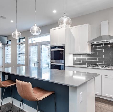 modern-columbus-kitchen-remodel-large-island-pendant-lighting Modern kitchen remodel featuring a large island with seating, glass pendant lighting, white cabinetry, built-in oven, and gray subway tile backsplash.