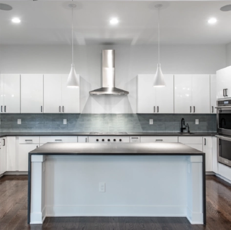 white-modern-kitchen-remodel-stainless-range-hood-large-island Bright modern kitchen remodel with white cabinetry, large island workspace, stainless steel range hood, and glass tile backsplash.